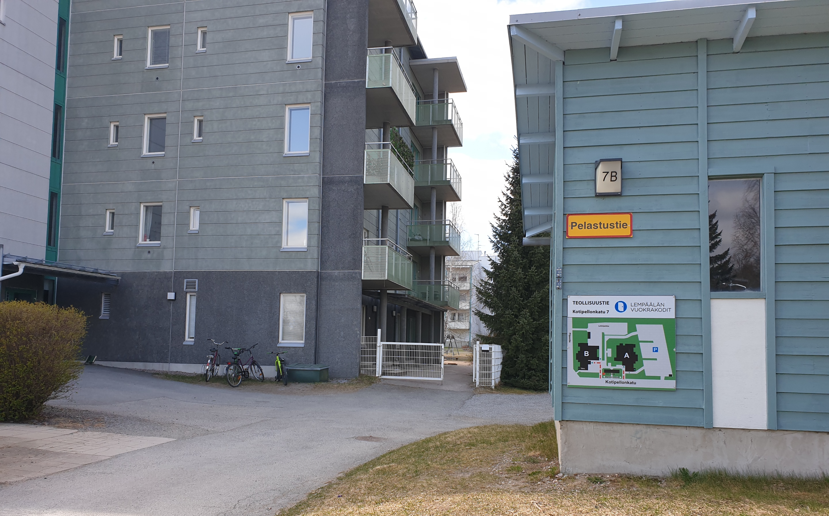 Korkean kerrostalon sisäänkäynti, oikealla varastorakennuksen seinässä kyltti, jossa on kartta.