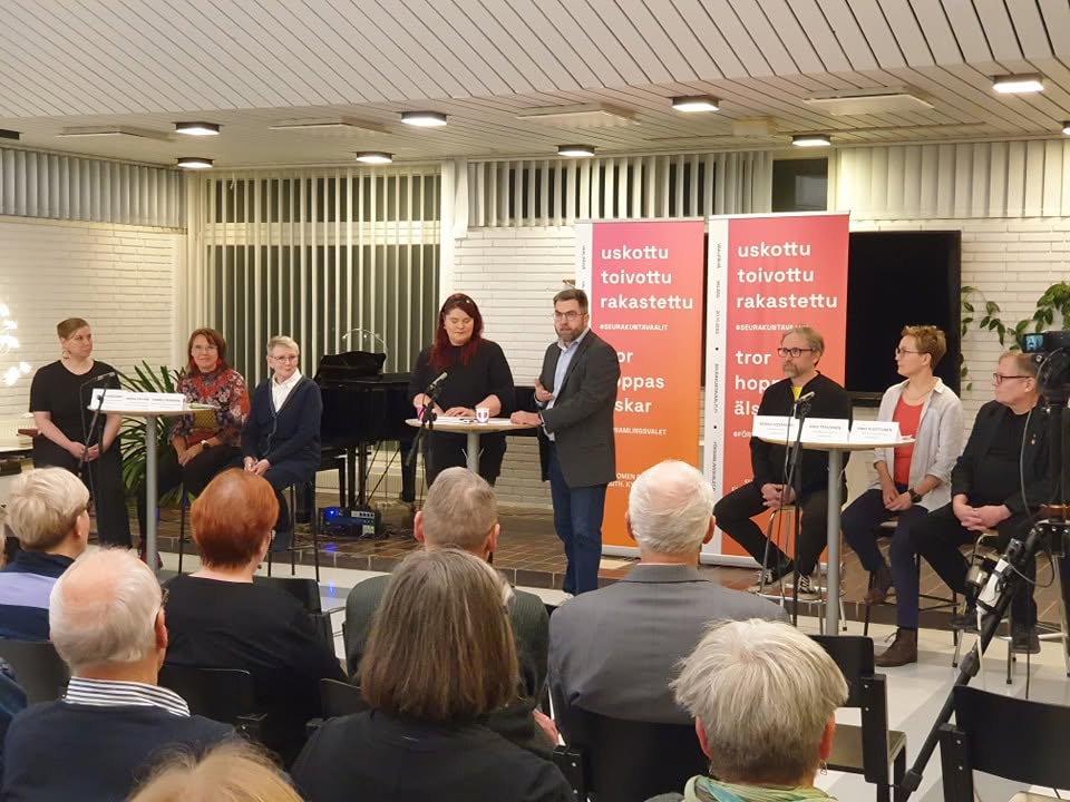 Vaalipaneeli, jossa keskellä kaksi juontajaa ja reunoilla ehdokkaita, edessä yleisöä.
