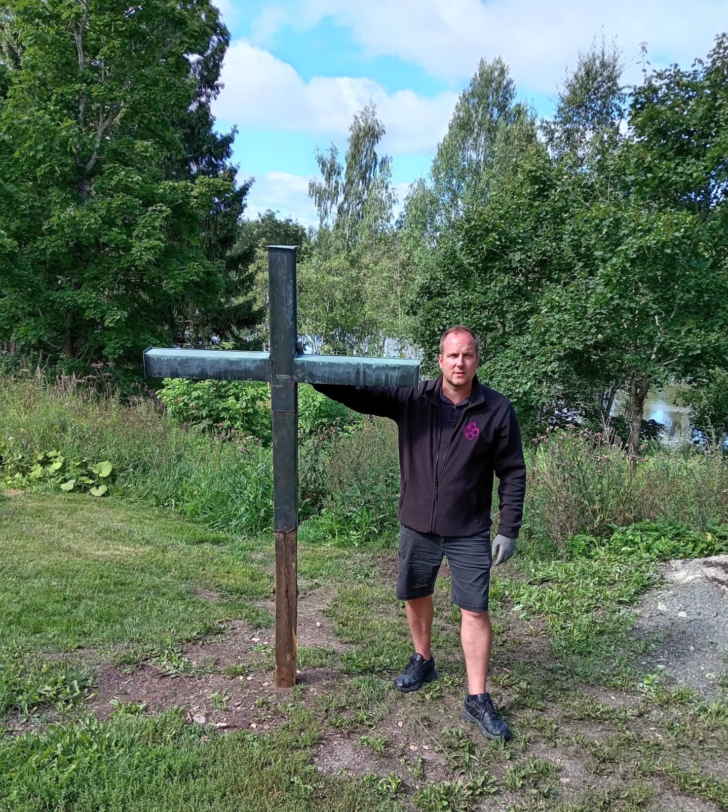 Mies ja risti, takana vesistö ja puustoa.