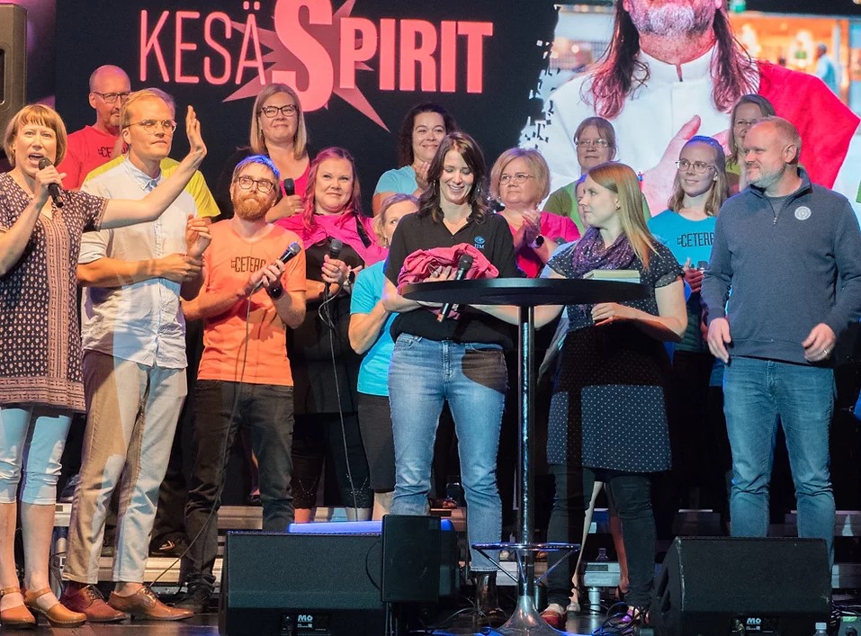 KesäSpirit -tapahtuman mainoskuva, jossa esiintymislavalla on paljon ihmisiä ja taustalla on tapahtuman logo.