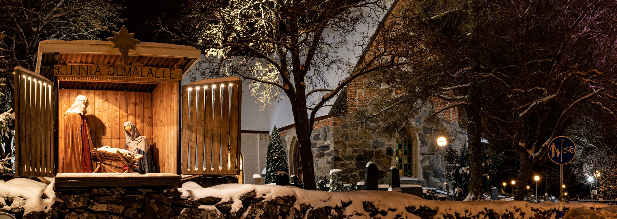 Luminen Lempäälän kirkko ja kirkon kiviaidalla oleva valaistu seimiasetelma joulun aikaan.