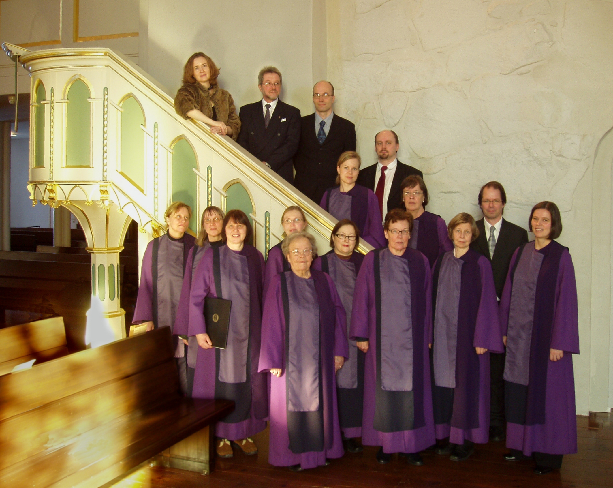 Violetteihin esiintymisasuihin pukeutunut kirkkokuoro Pyhän Birgitan kirkon saarnastuolin edessä.