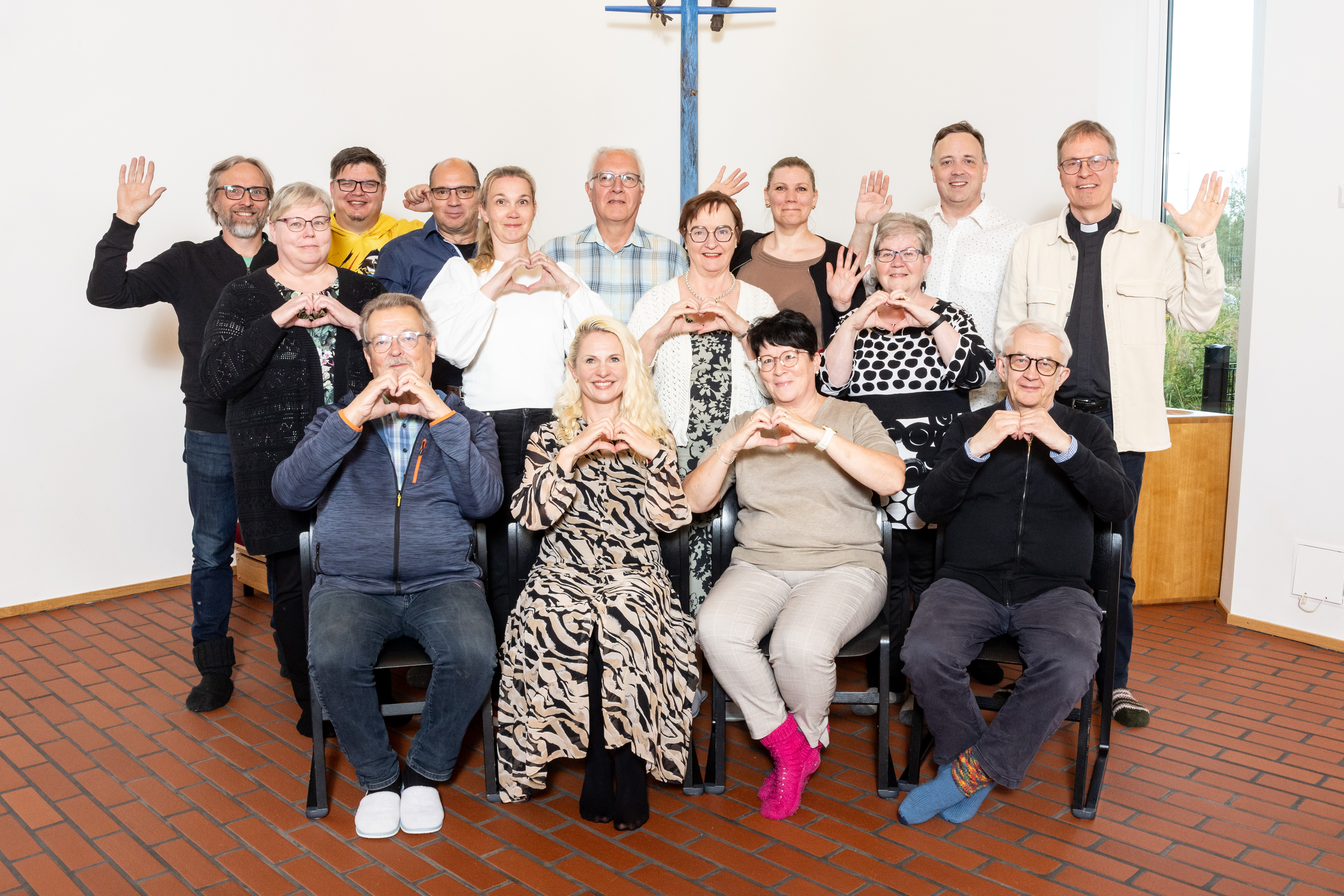 Lempäälän seurakunnan kirkkoneuvosto yhteiskuvassa, jossa jäsenet vilkuttavat ja tekevät käsillään sydänmer...