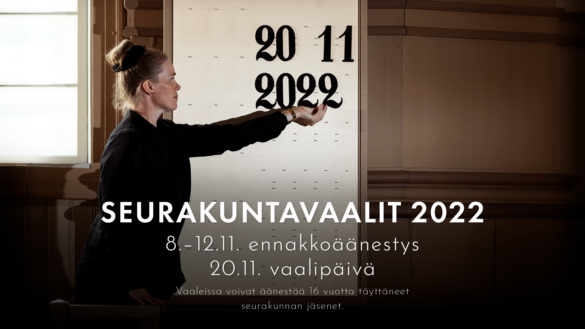 Seurakuntavaalien mainoskuva, jossa suntio asettelee virsitauluun numerot 20 11 2022 eli vaalipäivämäärän.