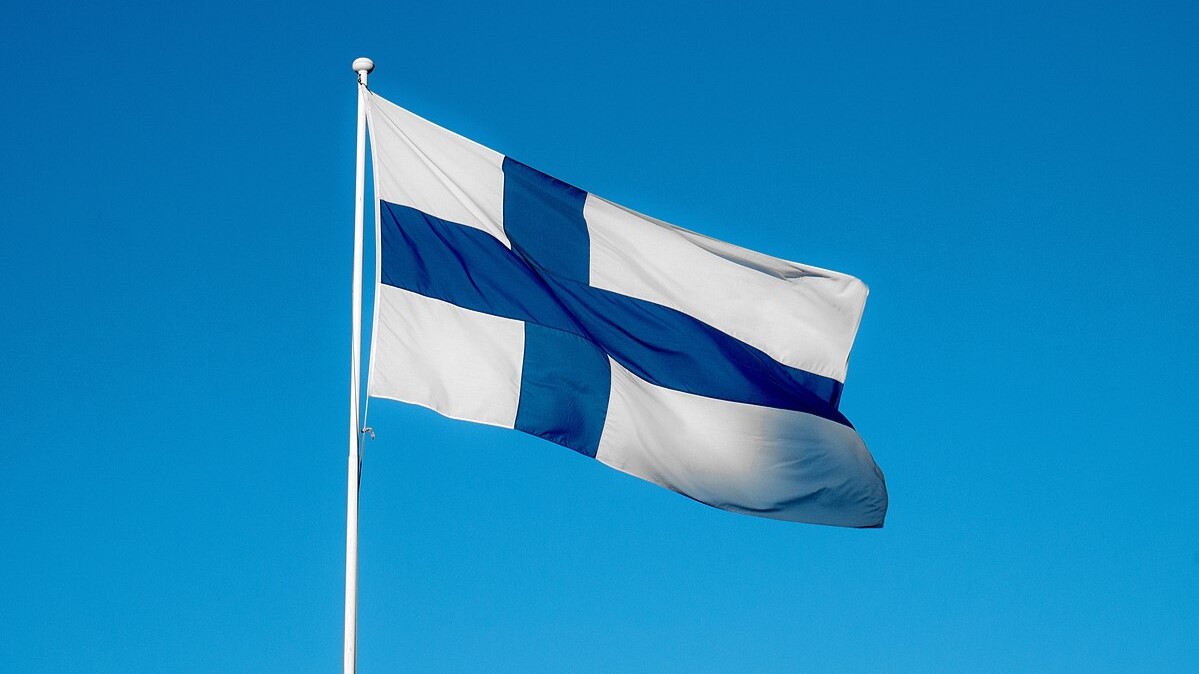 Suomen lippu liehuu sinistä taivasta vasten.