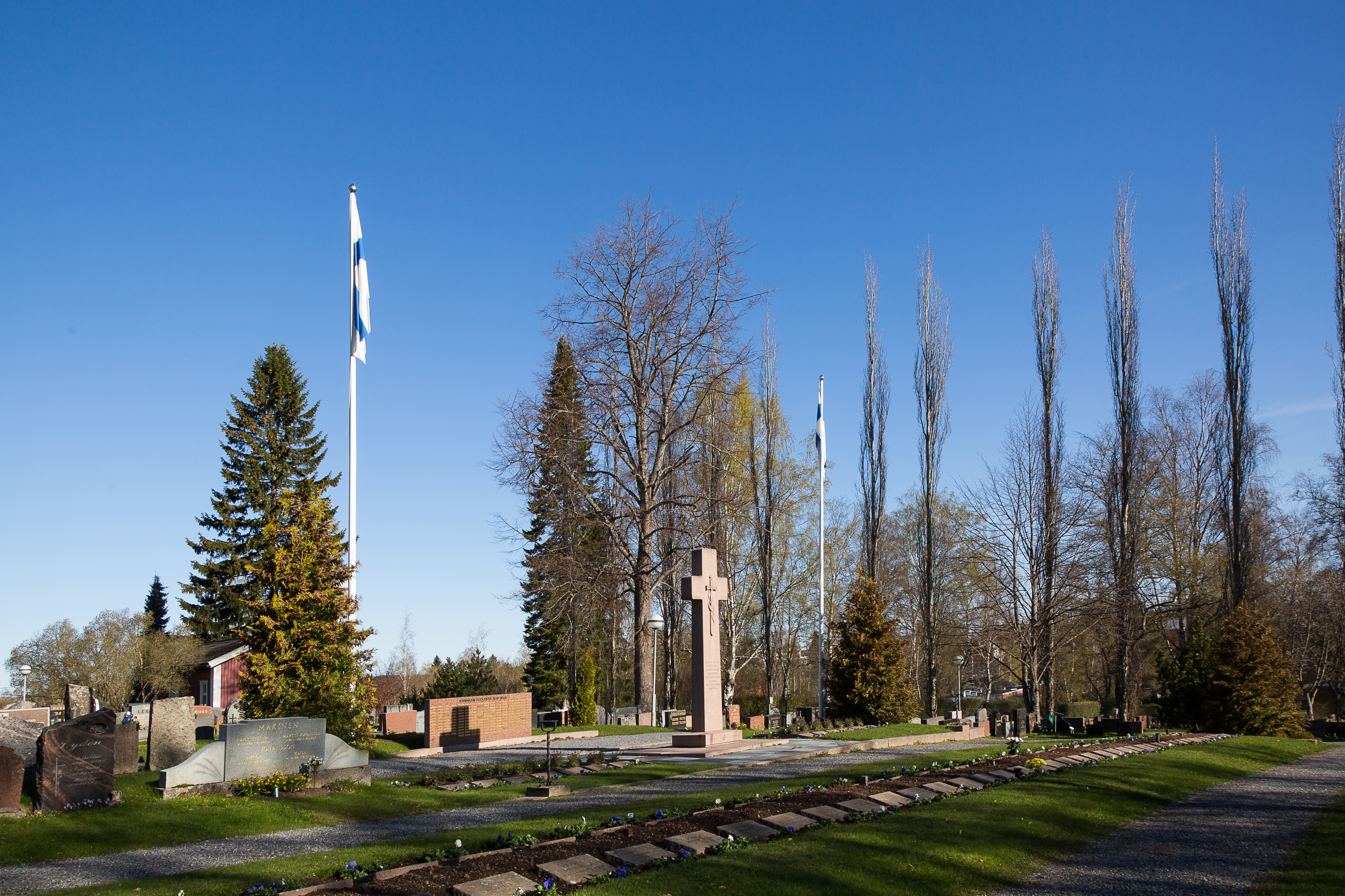 Lempäälän sankarihautausmaa, jossa ristin muotoisen muistomerkin vieressä lippusalko, jossa liehuu Suomen l...