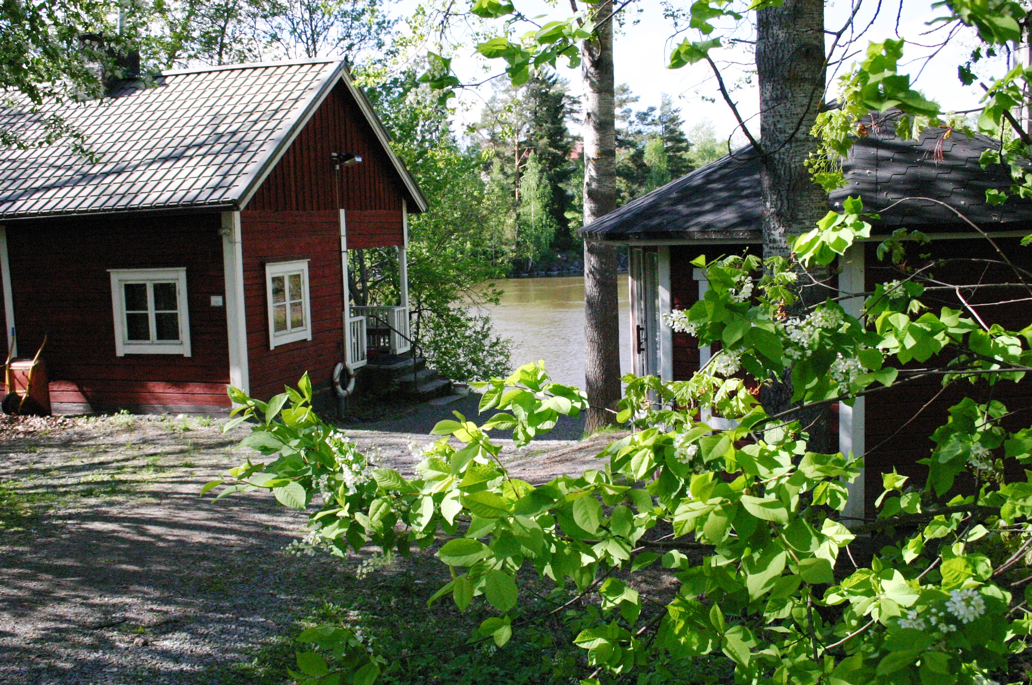 Punainen sauna ja grillikatos vesistön äärellä luonnon keskellä.