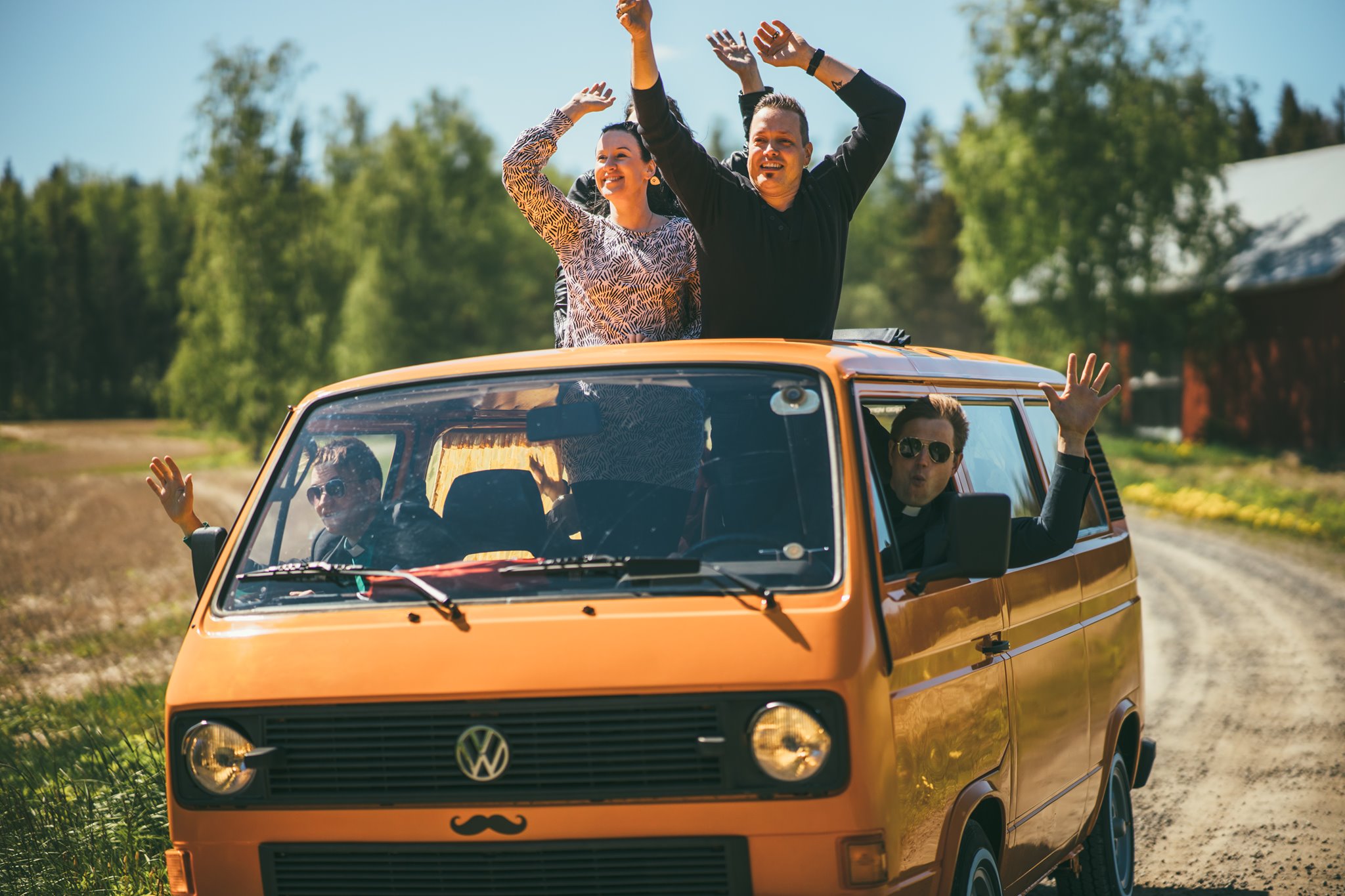 Kesä Spirit 2021 Ideaparkissa Oranssi auto maalaistiellä. Katto- ja sivuikkunoista huiskuttaa iloisia ihmisiä.