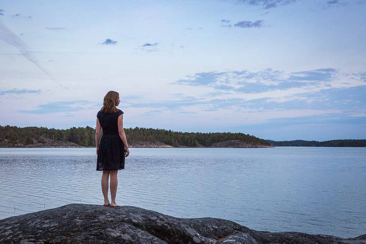 Uskon kuvat - Sonja Meskasen valokuvanäyttely Nainen seisoo järven rannalla, kalliolla, avaran taivaan alla ja katsoo kaukaisuuteen.