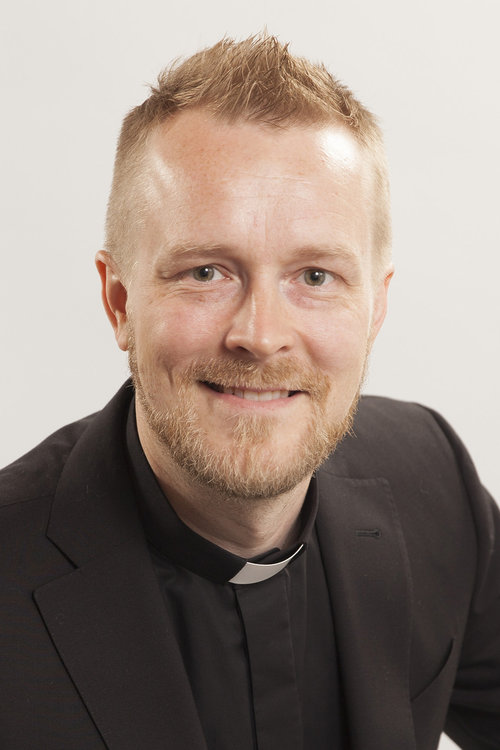 Seurakuntapastori Henri Karvinen hymyilee papinpaita yllään.