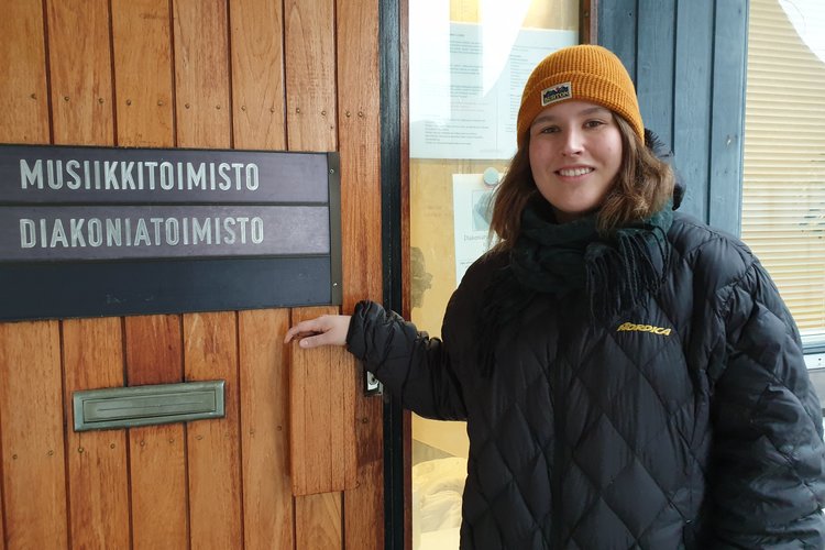 Keltapipoinen Liisa Nurminen avaa diakoniatoimiston oven. Ovessa on kyltti