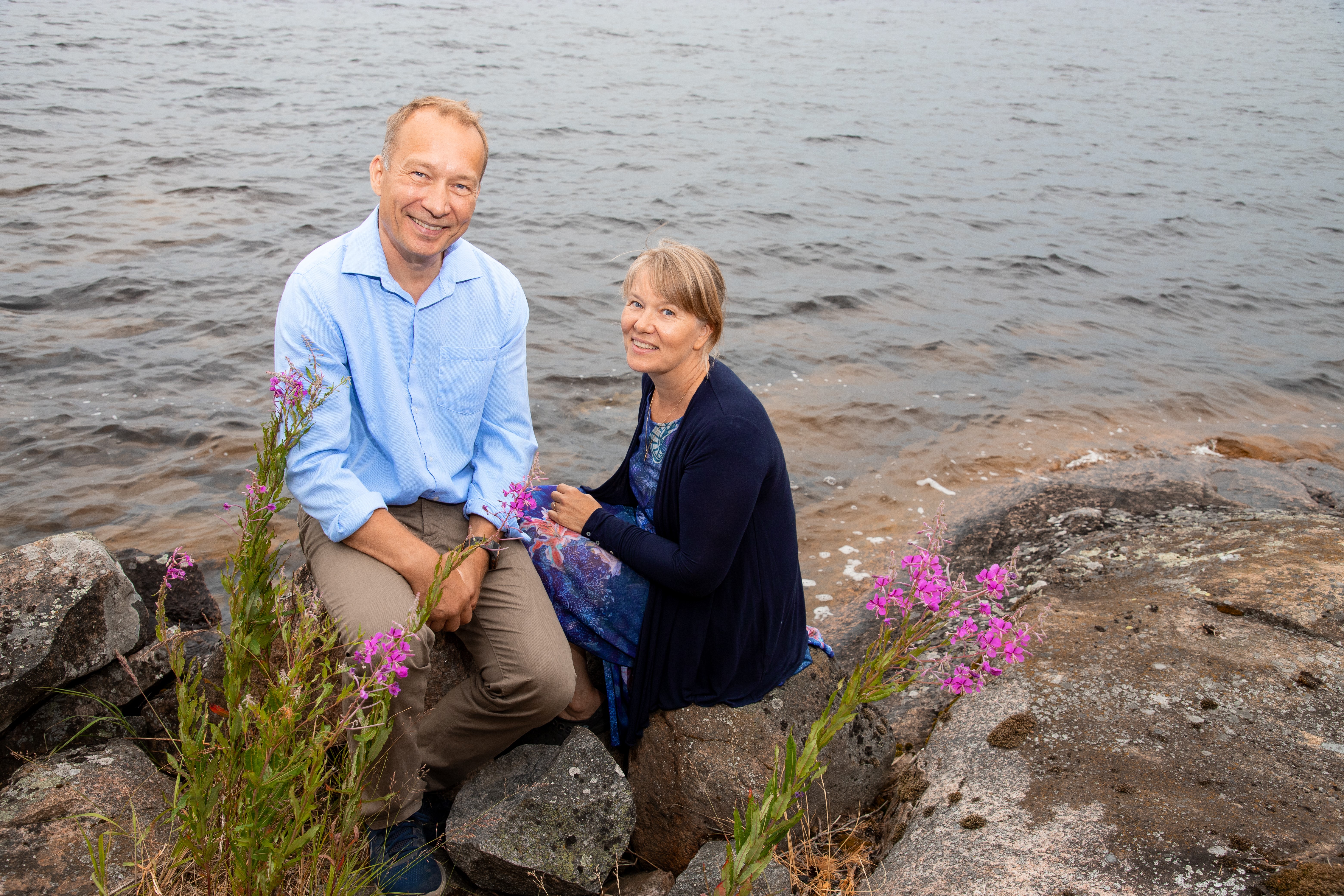 Mies ja nainen järven rannalla, kuvassa myös kukkia.