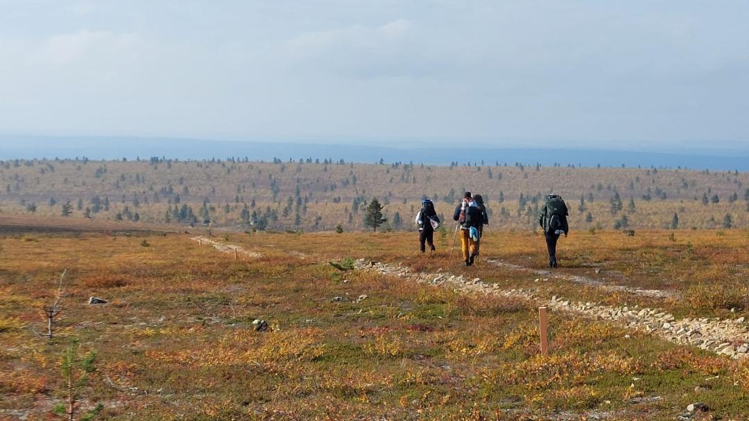 Kolme ihmistä vaeltaa puuttomassa syksyisessä avarassa maisemassa.