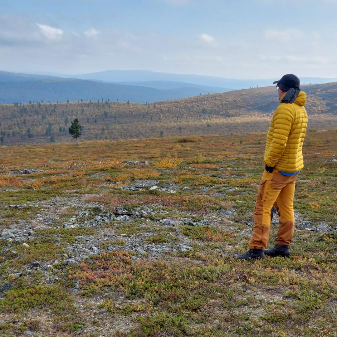Keltavaatteinen mies katselee paljasta tunturimaisemaa.