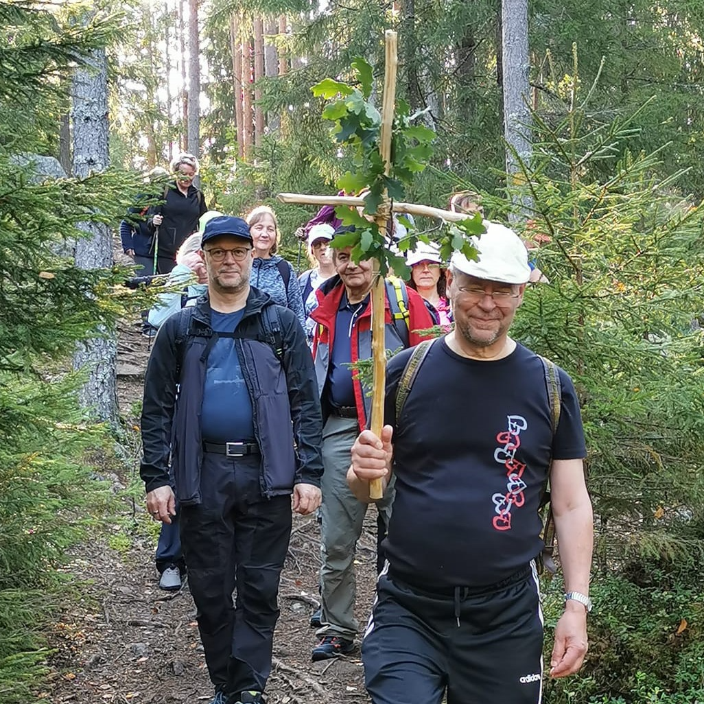 Ryhmä vaeltajia, joista etummaisella on kukin koristeltu risti. 